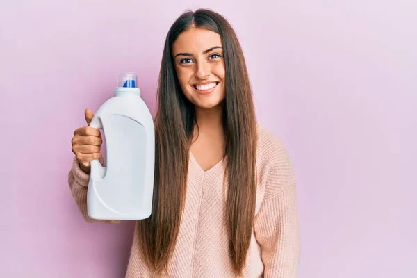 洗濯洗剤の瓶を持っている美しいヒスパニック系の女性はポジティブで幸せな立っていると歯を示す自信を持って笑顔で笑顔 — ストック写真