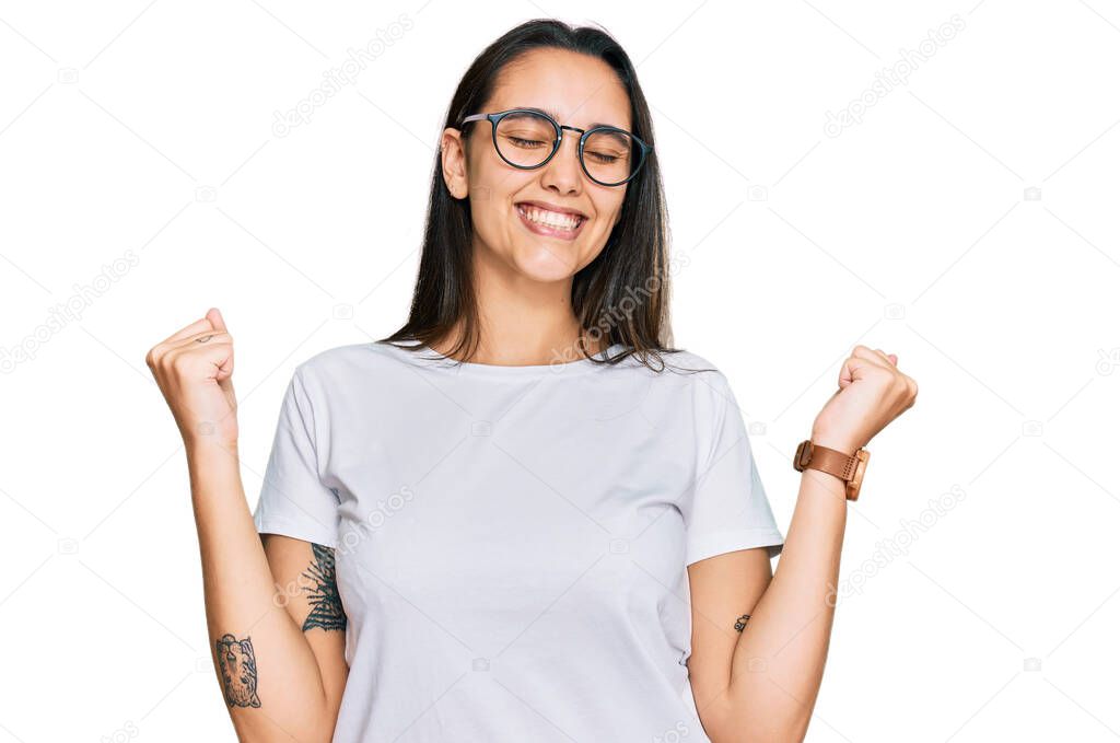 Young hispanic woman wearing casual white t shirt very happy and excited doing winner gesture with arms raised, smiling and screaming for success. celebration concept. 