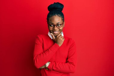 Genç Afro-Amerikalı kadın günlük kıyafetler giyiyor ve elleri çenesinde gözlük takıyor soru sormayı düşünüyor, düşünceli bir ifade. Düşünceli bir yüzle gülümsüyor. şüphe kavramı. 