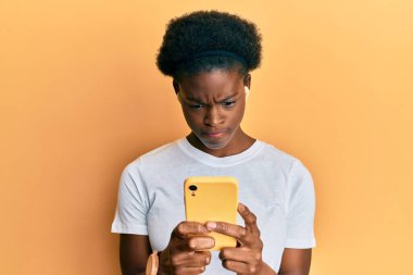 Genç Afro-Amerikalı kız akıllı telefon ve kulaklık kullanıyor. Kuşkucu ve gergin. Sorunlar yüzünden surat asıyor. negatif kişi. 