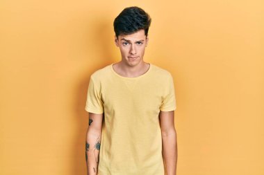 Sıradan sarı tişört giyen genç İspanyol adam şüpheci ve gergin, sorun yüzünden surat asıyor. negatif kişi. 