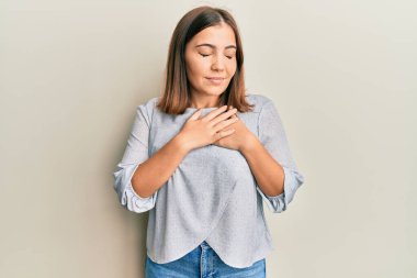 Elleri göğsünde gülümseyen sıradan kıyafetler giyen genç ve güzel bir kadın. Minnettar bir yüz ifadesiyle gözleri kapalı. sağlık kavramı. 