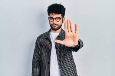 Sakallı, gözlüklü genç bir Arap avucuyla şarkı söylemeyi kesiyor. Yüzünde olumsuz ve ciddi bir jest olan uyarı ifadesi. 