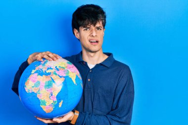 Dünya topunu tutan yakışıklı hippi genç adam bilgisiz ve kafası karışık bir ifade. şüphe kavramı. 