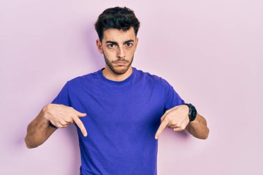 Gündelik tişört giyen genç İspanyol adam üzgün ve üzgün görünüyor, parmaklarıyla yönü gösteriyor, mutsuz ve depresif.. 