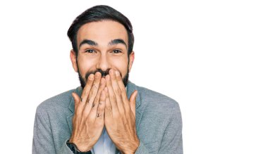 İş kıyafetleri giymiş genç İspanyol adam gülüyor ve utanıyor kıkırdıyor elleriyle ağzını kapatıyor, dedikodu yapıyor ve skandal konsepti yapıyor. 