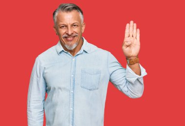 Orta yaşlı, gri saçlı, günlük kıyafetler giyen, dört numarayı gösteren ve gülümseyen, kendinden emin ve mutlu bir adam.. 