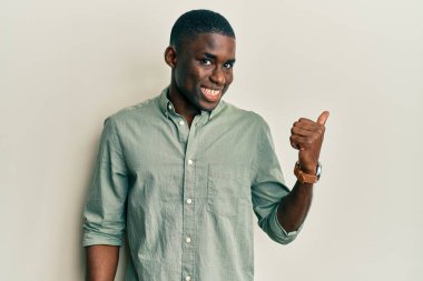 Genç Afro-Amerikalı günlük kıyafetler giymiş mutlu yüzüyle gülümseyen ve başparmağıyla yüzünü gösteren bir adam.. 