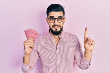 Elinde poker kartları olan yakışıklı bir adam bir fikirle gülümsüyor ya da mutlu bir yüzle bir numarayı işaret ediyor. 