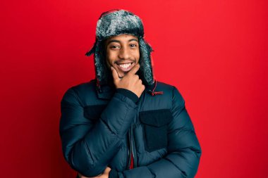 Sakallı, kışlık şapkalı ve paltolu genç Afro-Amerikan adam kameraya bakarken kollarını kavuşturmuş ve çenesini kaldırmış gülümsüyor. Olumlu düşünmek. 