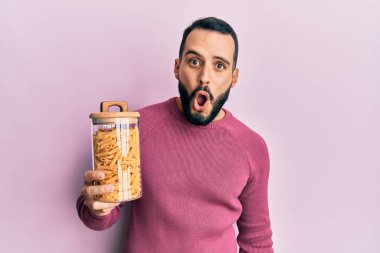 Sakallı genç adam elinde makarna kavanozuyla korkmuş ve ağzı açık şaşırmış, inançsız yüz. 