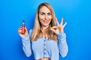 Genç beyaz kadın elinde elektronik sigara tutuyor. Parmaklarıyla imza atıyor, gülümsüyor. Mükemmel bir sembol. 