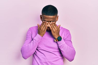 Genç siyah bir adam günlük pembe süveter giyiyor yorgunluk ve baş ağrısı için gözlerini ovuşturuyor, uykulu ve yorgun bir ifade takınıyor. görme sorunu 