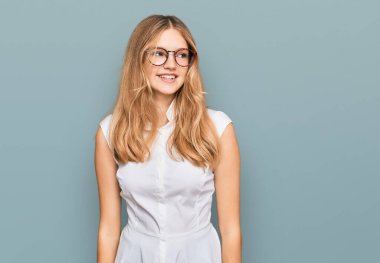 Gündelik kıyafetler ve gözlük takan güzel beyaz bir kız yüzünde gülümseme, doğal bir ifade ile yan yana bakıyor. Kendinden emin gülen. 