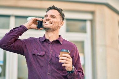 Genç İspanyol adam akıllı telefondan konuşuyor ve şehirde kahve içiyor..