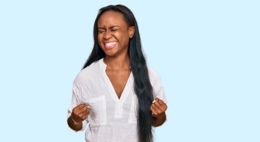 Başarı için heyecanlı, kolları havada, gözleri kapalı ve gülümseyerek zaferi kutlayan gündelik kıyafetler giyen genç siyahi kadın. Kazanan konsept. 