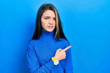 Balıkçı yaka kazak giyen genç esmer kız endişeli ve gergin bir şekilde işaret ediyor. 