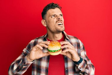 Lezzetli bir klasik burger yiyen genç bir İspanyol sinirli ve kızgın çığlıklar sinirli ve öfkeliydi, öfkeyle bağırıyordu. öfke ve agresif konsept. 