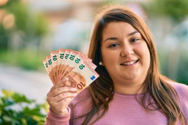 Genç İspanyol artı iri kadın gülümseyerek şehirde 10 avroluk banknotlar tutuyor..