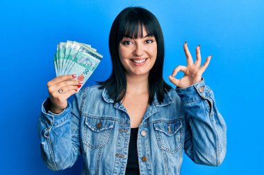 50 Malezya bankası tutan genç İspanyol kadın parmaklarıyla imza atıyor, gülümseyerek mükemmel bir sembol oluşturuyor. 