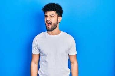 Sakallı, sıradan beyaz tişörtlü genç bir Arap sinirli ve öfkeli çığlıklar atıyor öfkeyle bağırıyor. öfke ve agresif konsept. 