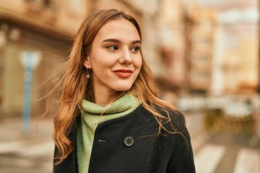 Genç sarışın kız gülümsüyor, mutlu bir şekilde şehirde duruyor..