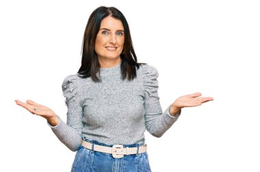 Orta yaşlı esmer kadın gündelik giysiler giyiyor, elleri ve kolları havada, kafası karışmış bir ifade takınıyor. şüphe kavramı. 