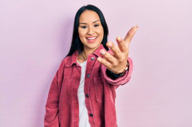 Güzel İspanyol bir kadın, burun piercingli, sıradan pembe bir ceket giyen, dostça gülümseyerek selamlama ve hoş geldin diyor. başarılı iş. 