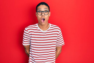 Genç Afro-Amerikalı adam günlük kıyafetler ve gözlük takıyor. Şaşırmak için ağzı açık kalmış, korkmuş ve şaşırmış. İnanmayan yüz. 
