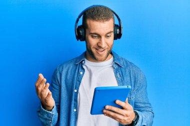 Dokunmatik kulaklık takan genç beyaz adam zaferi mutlu bir gülümsemeyle kutluyor ve kazanan el kaldırarak ifade ediyor. 