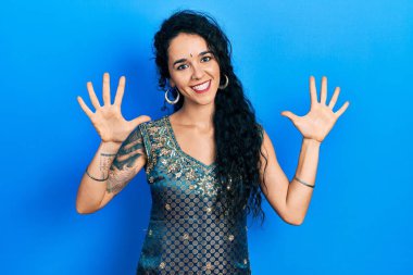Bindi ve geleneksel kurta elbisesi giyen genç bir kadın on numarayı gösterip işaret ederken kendinden emin ve mutlu bir şekilde gülümsüyor.. 