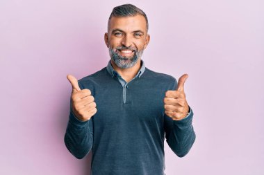 Orta yaşlı, sıradan giyinen yakışıklı bir adam. Başarı işareti yapıyor. Elinde olumlu bir jest yapıyor. Neşeli ifade ve kazanan jest. 