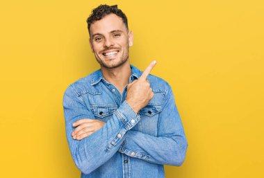 Yüzünde büyük bir gülümseme olan sıradan bir kot ceket giyen genç İspanyol adam, kameraya el ve parmak ile bakıyor.. 