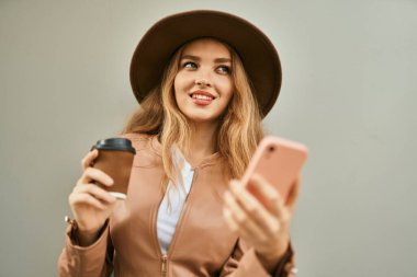 Genç sarışın kız akıllı telefon kullanıyor ve şehirde kahve içiyor..