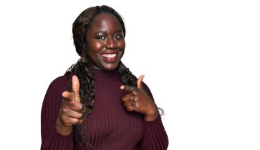 Kış süveteri giyen genç Afrikalı bir kadın mutlu ve komik yüzüyle kamerayı işaret ediyor. iyi enerji ve titreşimler. 