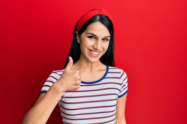 Neşeli ve pozitif gülümseyen Latin kökenli genç bir kadın. Başparmağıyla mükemmel ve onay işareti yapıyor. 