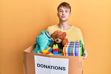 Genç, beyaz bir adam, elinde oyuncaklarla bağış kutusuyla kameraya bakıp öpüşürken çok güzel ve seksi görünüyor. aşk ifadesi. 