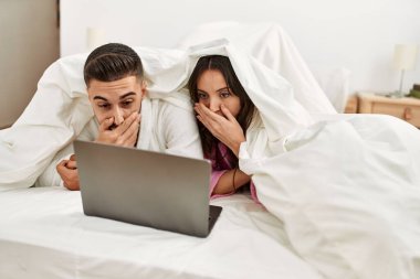 Yatakta dizüstü bilgisayar kullanarak film izleyen genç İspanyol çift..
