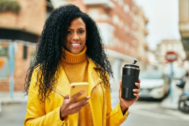Orta yaşlı Afro-Amerikan kadın akıllı telefon kullanıyor ve şehirde kahve içiyor..