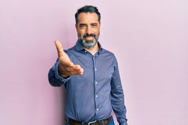 Orta yaşlı, sakallı, gri saçlı iş kıyafetleri giyen, dostça gülümseyerek selamlaşan bir adam. başarılı iş. 