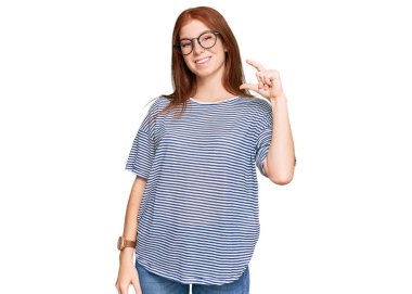 Gündelik kıyafetler ve gözlük takan, gülümseyen, kendine güvenen, el hareketi yapan, parmakları küçük gösteren ve kameraya bakan genç, okumuş bir kadın. ölçüm kavramı. 