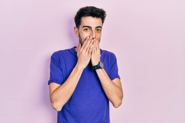 Gündelik tişört giyen genç İspanyol adam gülüyor ve utanıyor kıkırdıyor ağızları ellerle, dedikoduyla ve skandal konseptiyle örtüyor. 