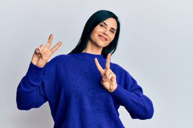 Gündelik giysiler giymiş genç beyaz kadın kameraya bakıp zafer işareti yapıyor. İki numara.. 