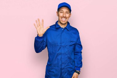 Sakallı, inşaatçı tulumu giyen kel bir adam beş numaralı parmaklarıyla kendini gösterip gülümserken mutlu ve kendinden emin.. 