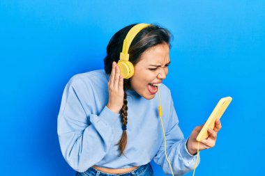 Genç İspanyol kız akıllı telefon ve kulaklık kullanıyor kızgın ve kızgın çığlıklar sinirli ve öfkeli, öfkeyle bağırıyor. öfke ve agresif konsept. 