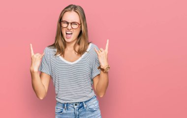 Güzel sarışın kadın, günlük kıyafetler ve gözlük takmış çılgın bir ifadeyle bağırıyor elleri havada rock sembolü yapıyor. Müzik yıldızı. ağır kavram. 