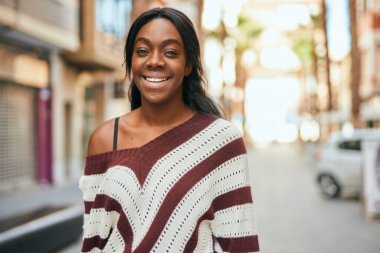 Genç Afrikalı Amerikalı kadın gülümseyerek şehirde mutlu mesut duruyor..