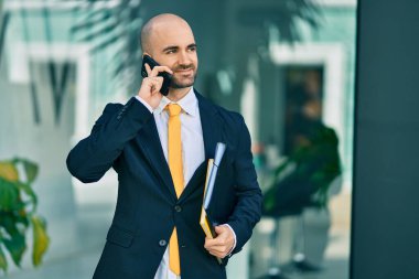 Genç Latin kökenli kel iş adamı gülümsüyor. Şehirdeki akıllı telefondan mutlu bir şekilde konuşuyor..