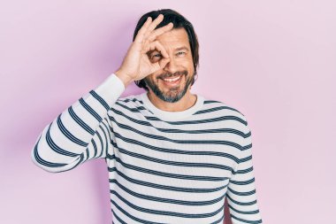 Orta yaşlı, günlük kıyafetler giyen, el hareketleriyle gülümseyen, mutlu yüzüyle parmaklarının arasından bakan beyaz bir adam.. 