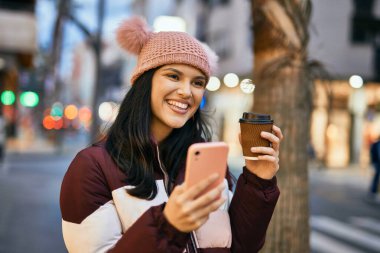 Genç İspanyol kız akıllı telefon kullanıyor ve şehirde kahve içiyor..